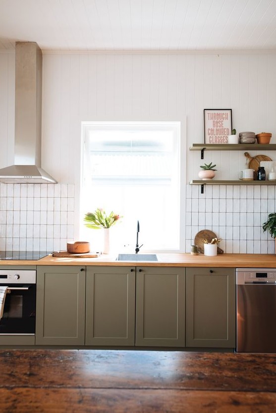 an olive green kitchen with wooden countertops, a white stacked tile backsplash and olive green shelves