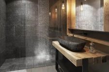 an ultra-modern chalet bathroom done with black stone tiles, a bit of blonde wood, blackened metal and a stone sink