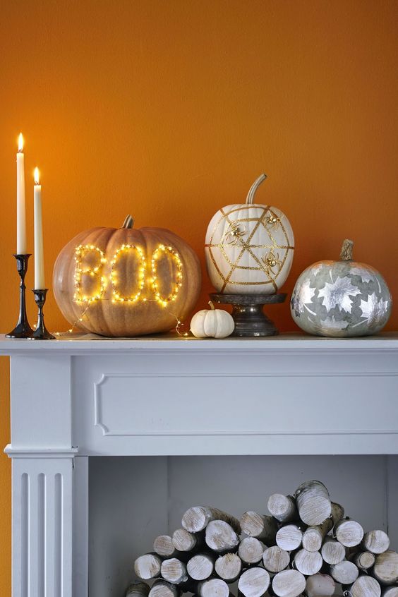 a lovely modern pumpkin arrangement of a pumpkin with lights, a white pumpkin with gold spiders and spider web, a grey pumpkin with silver leaves