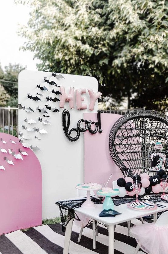 a pink, black and white Halloween party setting with paper bats, balloon letters and a black lace spiderweb runner