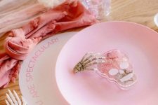 26 a pretty pink Halloween tablescape with a blush runner and a coral napkin, a pink plate and a skull and a skeleton hand is amazing