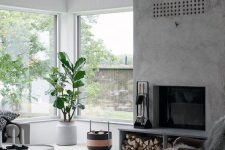 a Scandinavian living room with a concrete fireplace, neutral seating furniture, potted plants and printed textiles