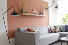a Scandinavian living room with a terracotta accent wall, a grey corner sofa, black lamps and a coffee table