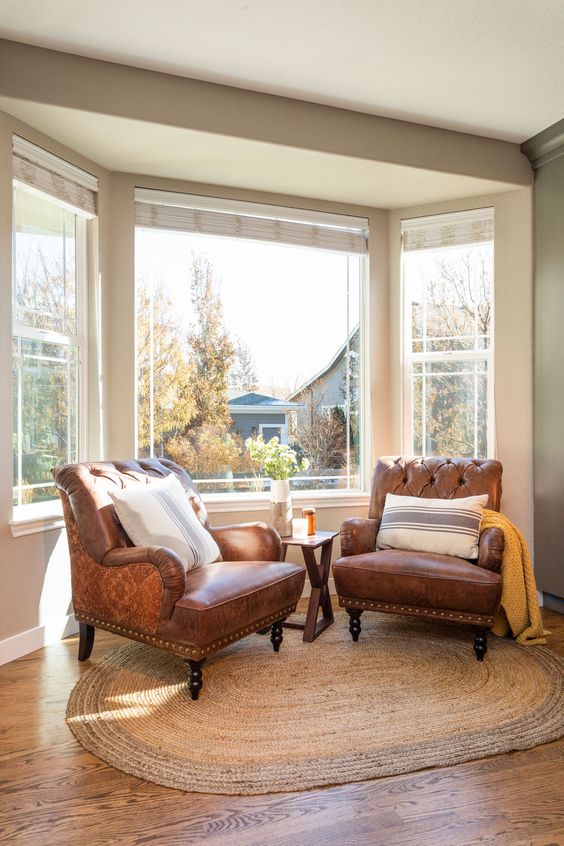a bay window styled as a sitting nook, with leather chairs, a coffee table, some pillows and a lovely view is amazing