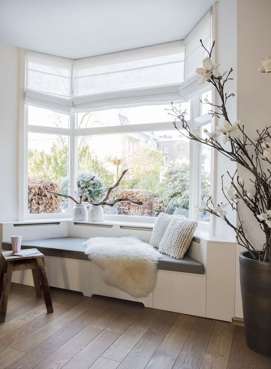 a bay window taken by a contemporary day bed, with pillows and faux fir, with some driftwood in vases is a cool reading nook