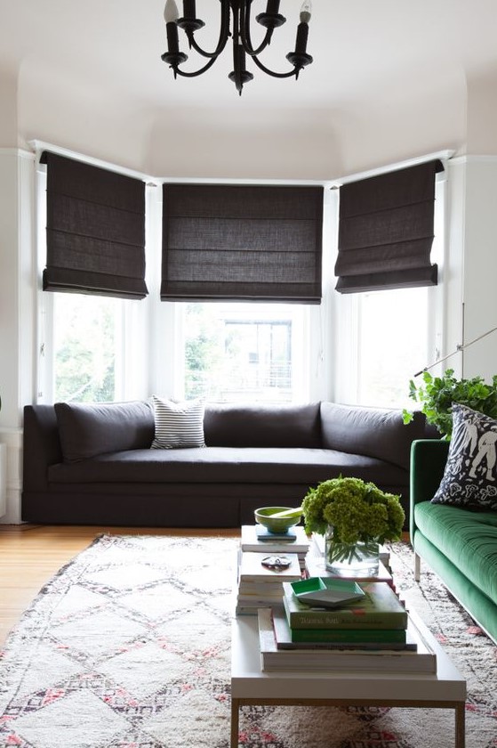 a bay window with a fitted sofa and pillows, dark shades makes this space cozy to be and welcomes a lot