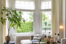a beautiful bay window area done with a lovely daybed with lots of pillows, a couple of side tables, greenery and a lovely view