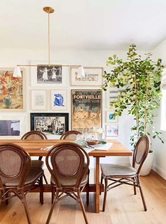a beautiful eclectic dining room with a stained table and vintage chairs, a potted tree and a free form gallery wall with much color