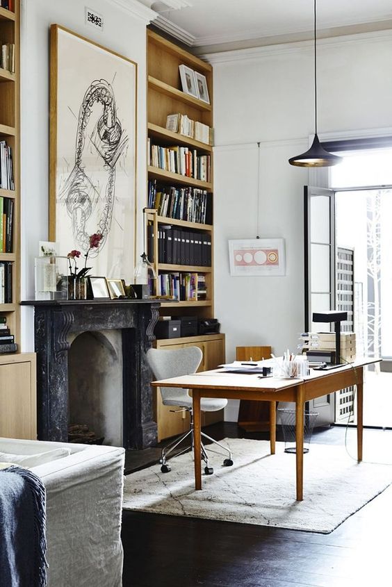 a beautiful modern Victorian home office with built-in bookcases, a non-working fireplace,a  simple and a neutral chair, a black pendant lamp