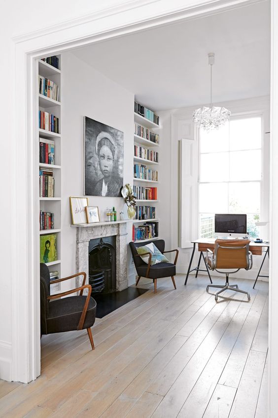 a beautiful modern home office in white, with built-in bookshelves, a fireplace with a marble surround, a stylish desk and black and beige chairs
