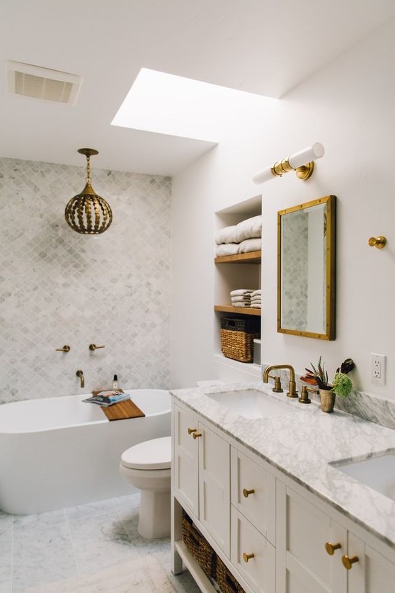 a beautiful neutral bathroom clad with marble subway and arabesque tiles, with a skylight, a large vanity and a pretty gilded pendant lamp