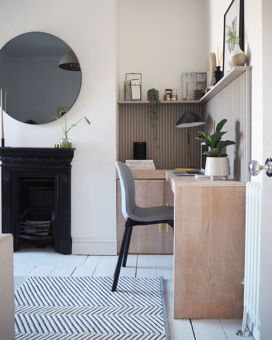 a beautiful neutral home office with a metal fireplace, a neutral corner desk, a grey chair, a long shelf, a round mirror and a printed rug