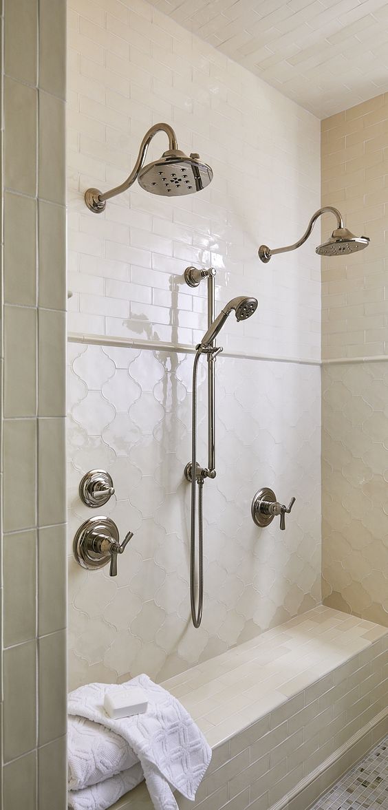 a beautiful neutral shower space clad with creamy skinny and arabesque tiles, with vintage fixtures and a built in bench
