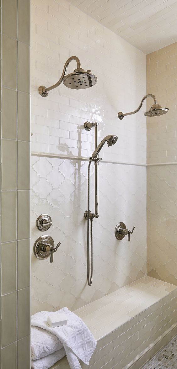 a beautiful neutral shower space clad with creamy skinny and arabesque tiles, with vintage fixtures and a built-in bench