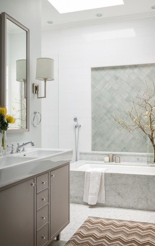 a beautiful serene bathroom with a skylight, a neutral vanity, a bathtub clad with stone, mint green arabesque tiles for an accent