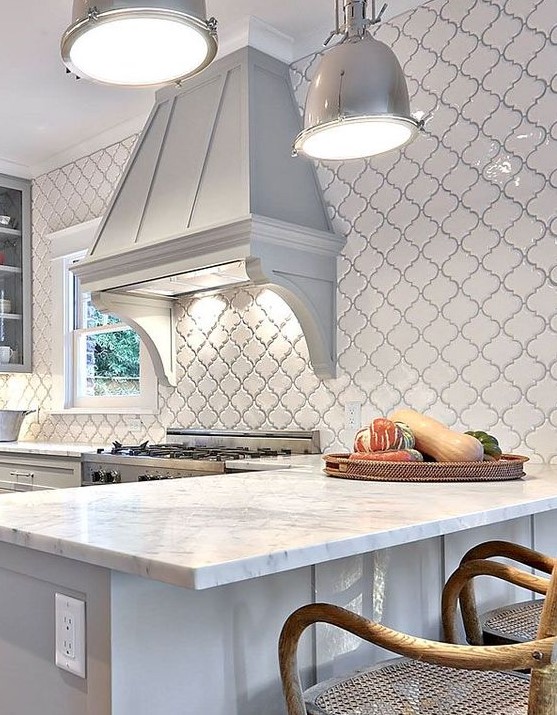 a beautiful vintage dove grey kitchen with glass cabinets, white stone countertops, a vintage greyhood and a wall clad with white arabesque tiles