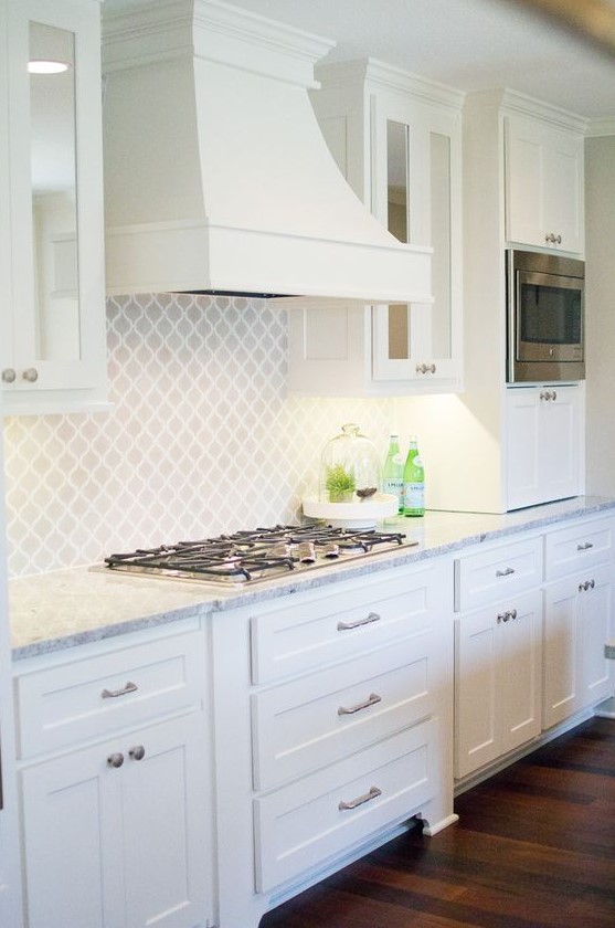 a beautiful white farmhouse kitchen with a matching white arabesque tile backsplash and a vintage hood is a lovely space