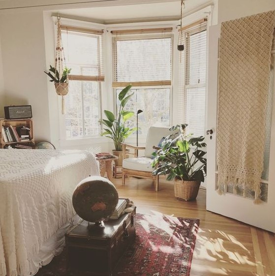a boho bedroom with a bay window, a chair and some potted plants, the window area is a very cozy nook