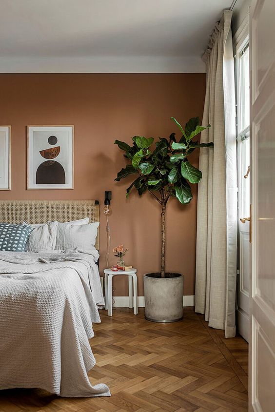 a boho bedroom with a terracotta accent wall, a bed with a woven bedding, a potted plant and a stool as a side table