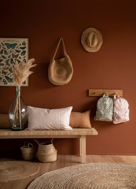 a boho entryway with a terracotta wall, a woven bench and a rack, some baskets and pampas grass in a large bottle