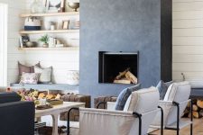 a bold and catchy living room in neutrals, with a grey concrete fireplace and benches with niches for storing firewood