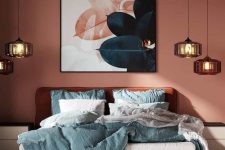 a bold and eye-catchy bedroom with terracotta walls, a burnt orange bed with blue bedding, clusters of pendant lamps and a bold artwork