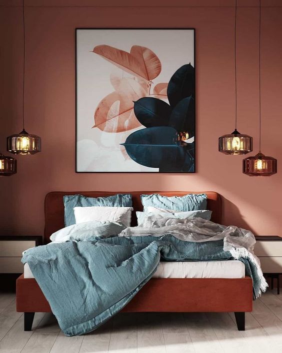 a bold and eye catchy bedroom with terracotta walls, a burnt orange bed with blue bedding, clusters of pendant lamps and a bold artwork