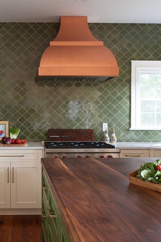 a bold kitchen with neutral shaker style cabinetry, a green arabesque tile backsplash, an orange hood and a green kitchen island with butcheblock countertops