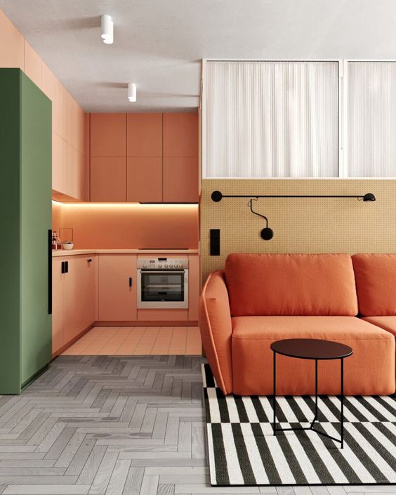 a bold modern space with an orange kitchen with built in lights and a green fridge, a burnt orange sofa and a striped rug