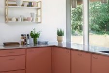 a bold rust-colored kitchen with grey countertops, an open shelf, green pendant lamps and potted greenery