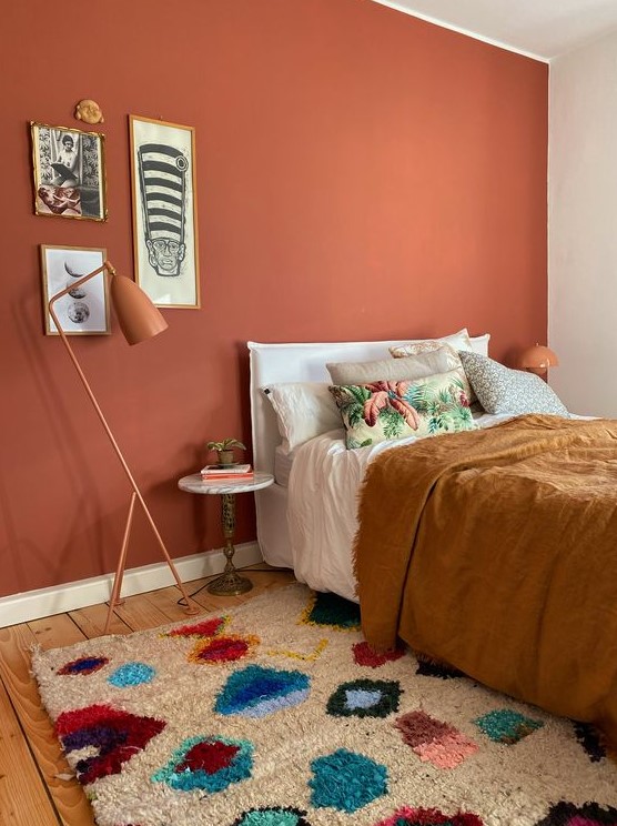 a bright bedroom with a terracotta accent wall, a white bed with eclectic bedding, a gallery wall and rust-colored lamps