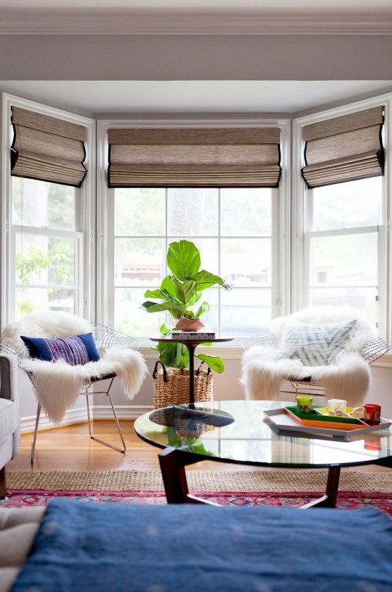 a bright boho sitting zone by the bay window - metal chais with pillows and faux fur, a potted plant and a window with Roman shades