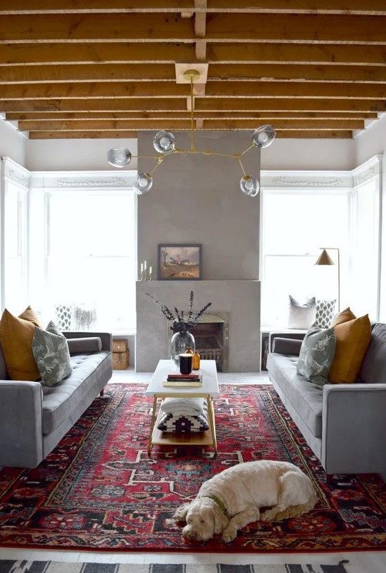 a bright living room done in grey and yellow, with grey sofas and mustard pillows, a concrete fireplace and a yellow chandelier