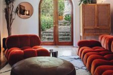 a catchy interior with bold rust-colored seating furniture, a leather ottoman, a copper mirror and a rattan sideboard