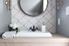 a chic and refined bathroom in neutrals, with grey walls and a white arabesque tile accent wall, a round mirror, chic sconces is amazing