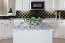 a chic modern white kitchen with shaker cabinets, white stone countertops, a black arabesque tile backsplash and greenery