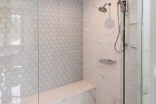 a chic neutral shower space clad with hex, marble and arabesque tiles, with a built-in bench and stainless steel fixtures