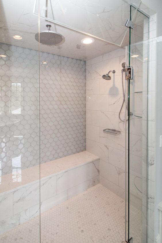 a chic neutral shower space clad with hex, marble and arabesque tiles, with a built-in bench and stainless steel fixtures