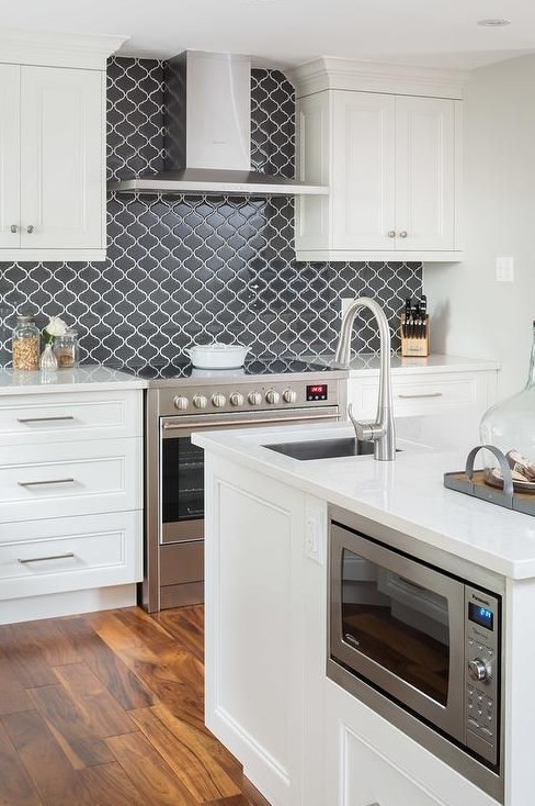 a chic white kitchen with shaker style cabinets, a graphite grey arabesque tile backsplash for a contrast and elegantly built-in appliances
