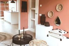 a cozy foyer with a terracotta accent wall, simple cabinets, round tables, a woven lamp and a small gallery wall