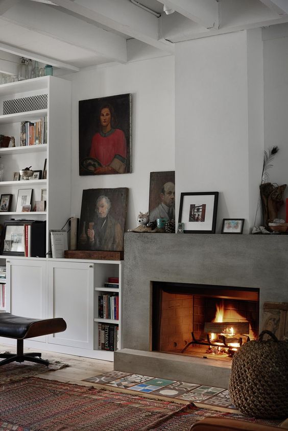 a cozy modern living room in neutrals, with a concrete fireplace, a colorful tile piece on the floor, printed rugs and artwork