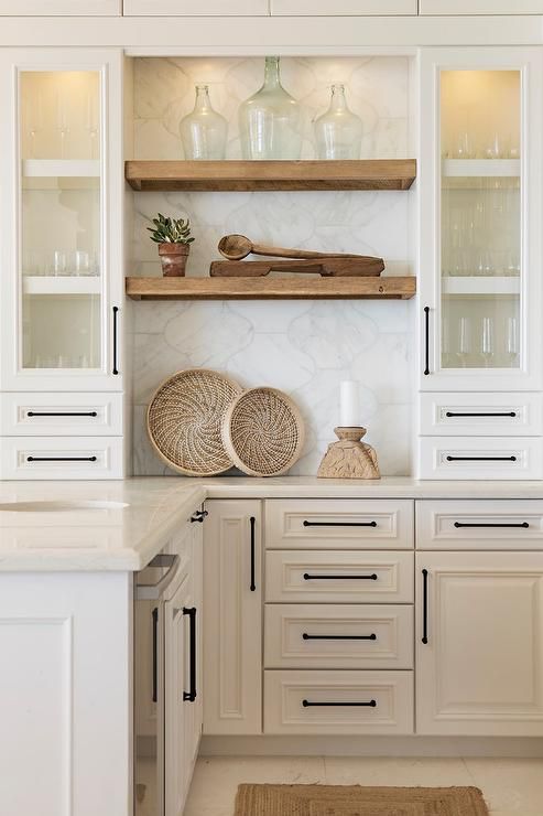 a creamy-colored kitchen with shaker style cabinets, lit up shelves and a large scale arabesque tile backsplash