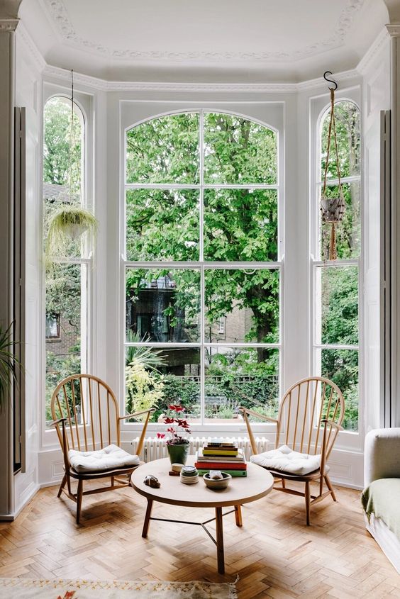 a floor to ceiling bay window with a couple of vintage chairs, a matching round table is a gorgeous conversation zone