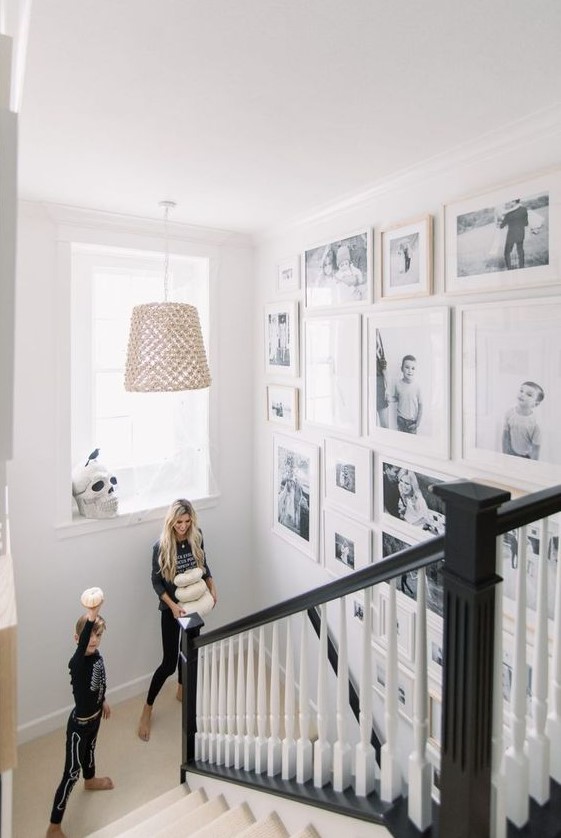 a free form gallery wall with black and white family pics and white frames is a very chic and stylish idea for any space