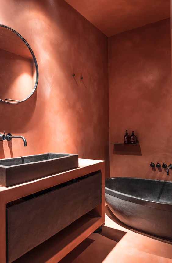 a jaw-dropping terracotta bathroom with a built-in vanity, a dark stone sink and a drawer, an oval tub and black fixtures