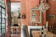 a jaw-dropping terracotta dining room with French windows, a fireplace, textural walls, a stained table and grey chairs plus crystal chandeliers