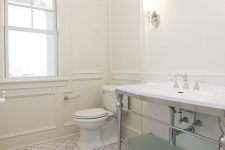 a large neutral vintage bathroom with paneled walls, white marble arabesque tiles on the floor, a large sink stand and a printed ceiling