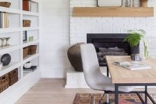 a lovely modern farmhouse home office with a white brick fireplace, a mantel, a large shelving unit with sconces, a delicate desk and printed rug