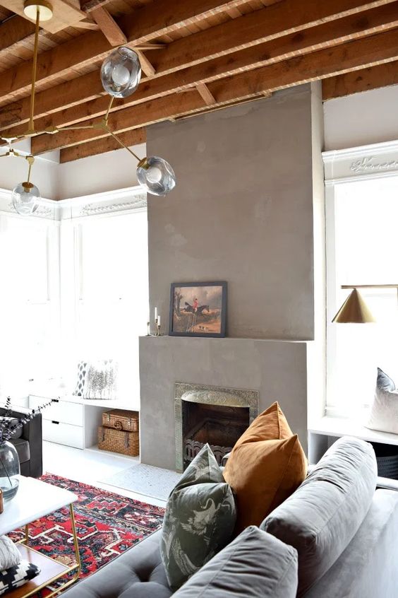 a mid-century modern living room with a concrete fireplace, grey seating furniture, printed textiles, a chic chandelier and a coffee table