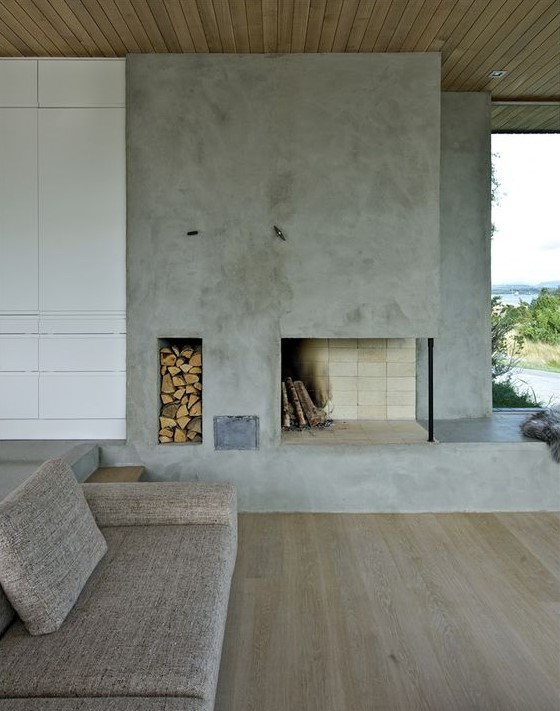a minimalist living room with a concrete fireplace, a niche for firewood storage and simple furniture